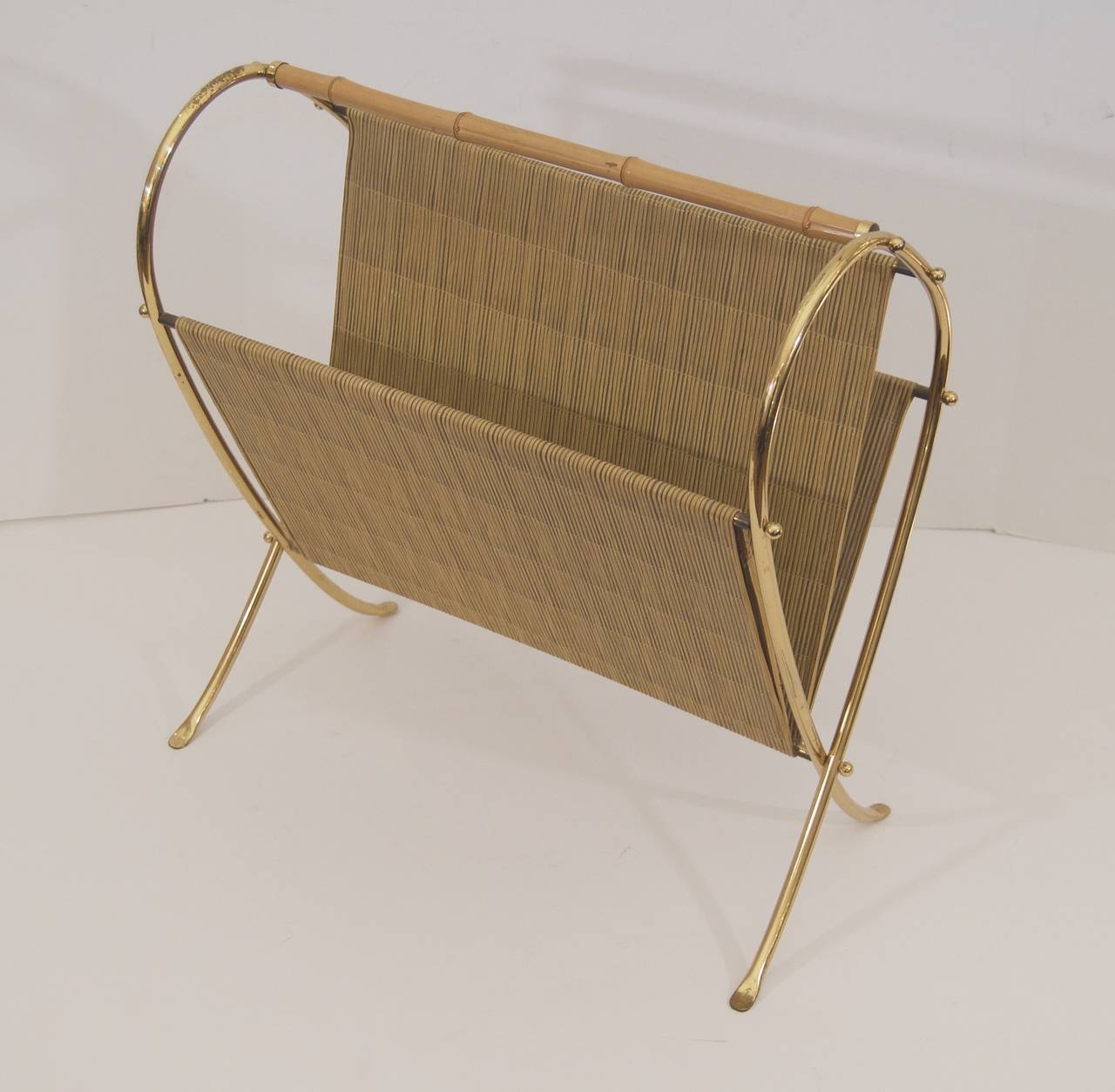 Magazine stand in brass with round ball finials and a bamboo handle. Pieces of faux bamboo wraparound the frame to create a receptacle for newspapers and books.