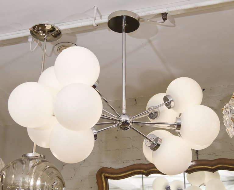 Twelve-armed chrome sputnik chandelier in a very unusual oblong form, two groups of six globes radiating longitudinally from the central body. Each arm capped by a matte finish opal glass globe. 

Suits a wide variety of interiors, and