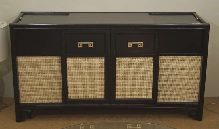 A very nicely sized piece in black lacquer with caned panels and greek key motif door handles. Originally a stereo cabinet, the center doors open to reveal central storage. On top, left and right sides slide back to reveal storage area. Shelf can be