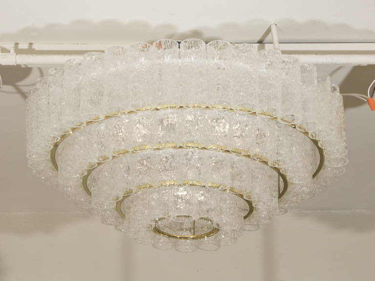 Stunning Doria four tier chandelier, each tier with an inset brass ring separating levels of individually hung blown glass tubes. Exquisite design and well suited for a variety of spaces.

Takes six E-14 base bulbs up to 40 watts each in central