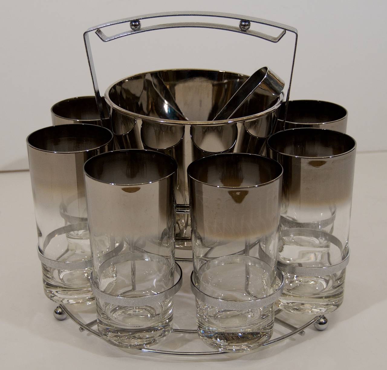Excellent bar glass set, 8 12 ounce tumbler glasses in chrome carrier, with central ice bucket and ice tongs in an octagonal form.