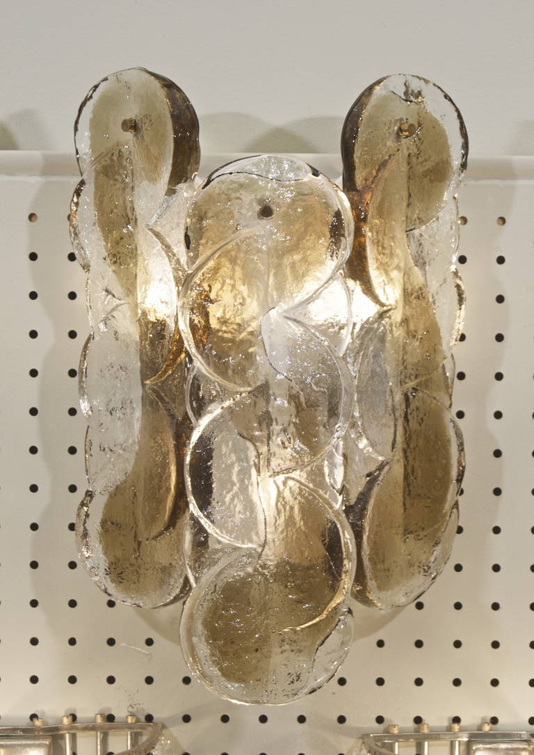 Excellent Kalmar sconces with three pieces of swirl patterned glass per sconce; the heavy glass pieces having a fused smoke or amber tone design similar to a violin F hole. Visible portion of backplate is white enamel, mounted with brass
