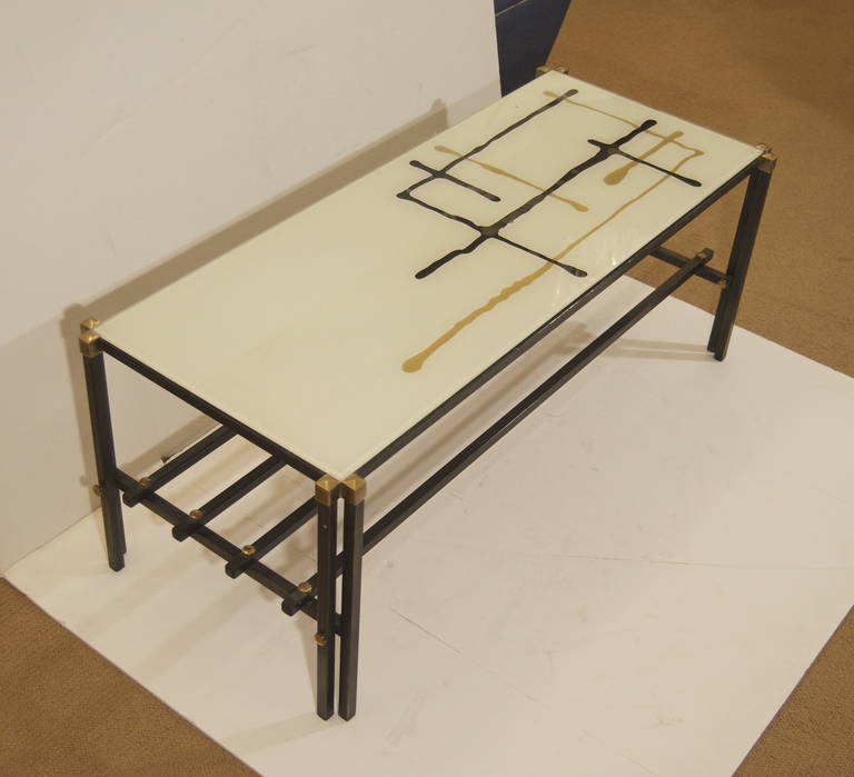 Unique and chic coffee table. A stylish Italian mid century modern coffee table, the body of black enameled metal with brass accents and a lower stretcher shelf, and the top of reverse painted glass with an unusual abstract geometric yet organic