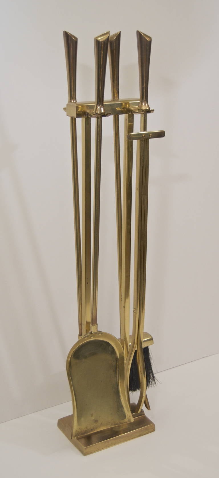 A streamlined fireplace tool set in brass reminiscent of Deskey designs.