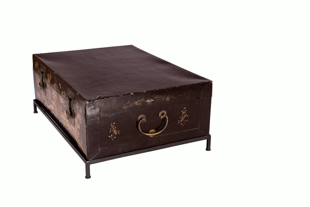 The delightful gold leaf designs on this Chinese leather trunk provide wonderful detail to this low coffee table. Set atop a 20th century metal base. 

This would work well as a cocktail table or side table in an entertaining space.