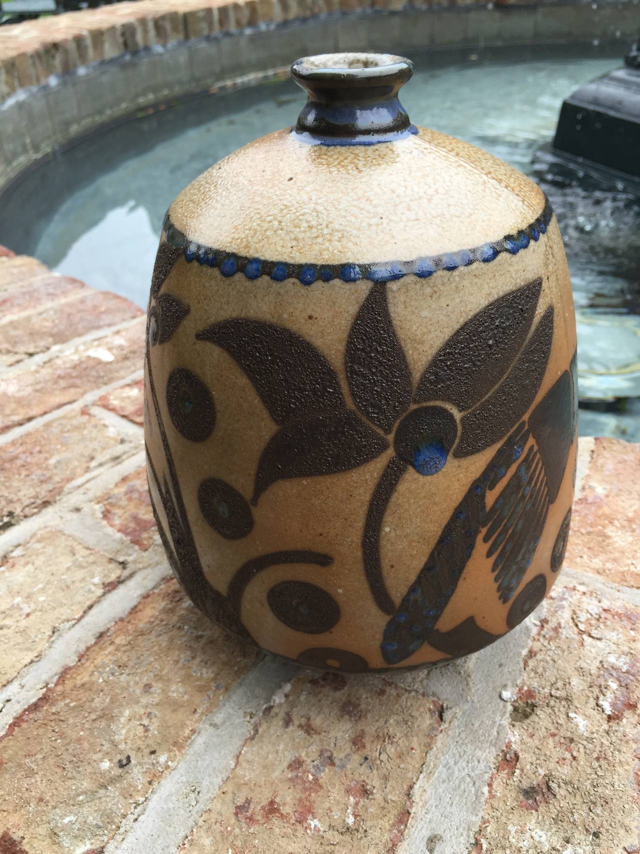 Glazed finish on this beautifully adorned ceramic vase in light brown and blue hues. Depicting birds and geometric shapes.