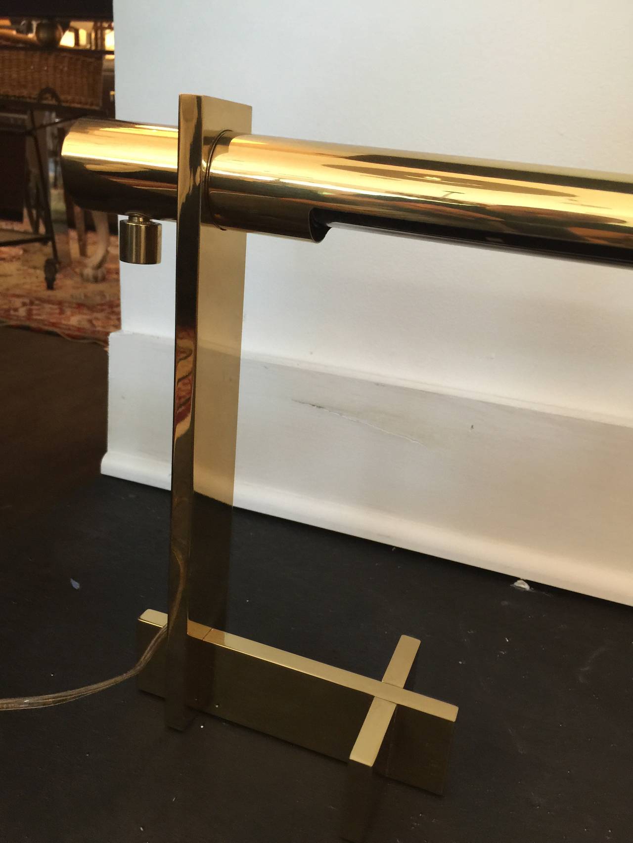 A chic desk lamp with an adjustable pivoting tubular shade and integral dimmer switch supported on a solid brass bar cross base. With manufacturer's label to base. By Casella Lighting, American, circa 1970.