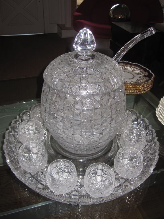 Beautifully cut crystal punch bowl with the original crystal ladle and twelve matching cups standing on a large platter.