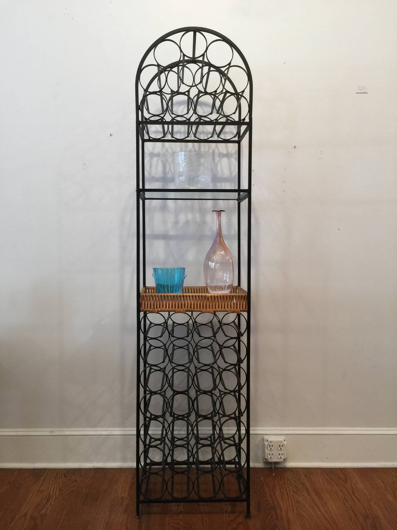 Tall iron wine rack, with cane basket and glass shelf, designed by Arthur Umanoff for Howard Shaver. Designed in the late 1960s, very functional wine rack holds 39 bottles along with display and storage for glasses and other related objects.