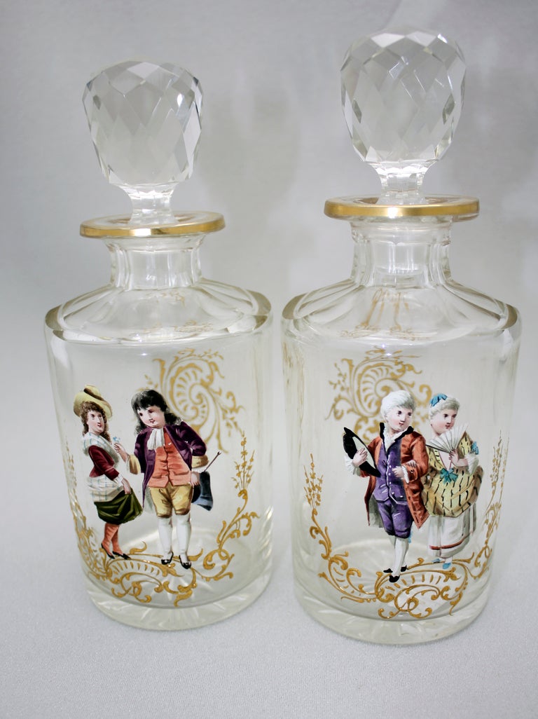 This pair of handblown crystal dresser bottles are panel cut and decorated with two pairs of hand-painted couples in period dress. The bases are star-cut, the stoppers are cut with a complex facet pattern and they are further embellished with raised