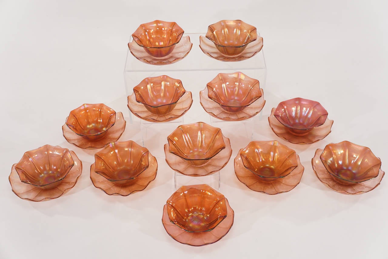 A perfect set of 12 Art Nouveau hand blown bowls and matching under plates made by Loetz. Each piece is an organically rib-shaped octagon with gold and pinkish palette. The overall iridescence gives them a bright glow and each has a polished pontil.