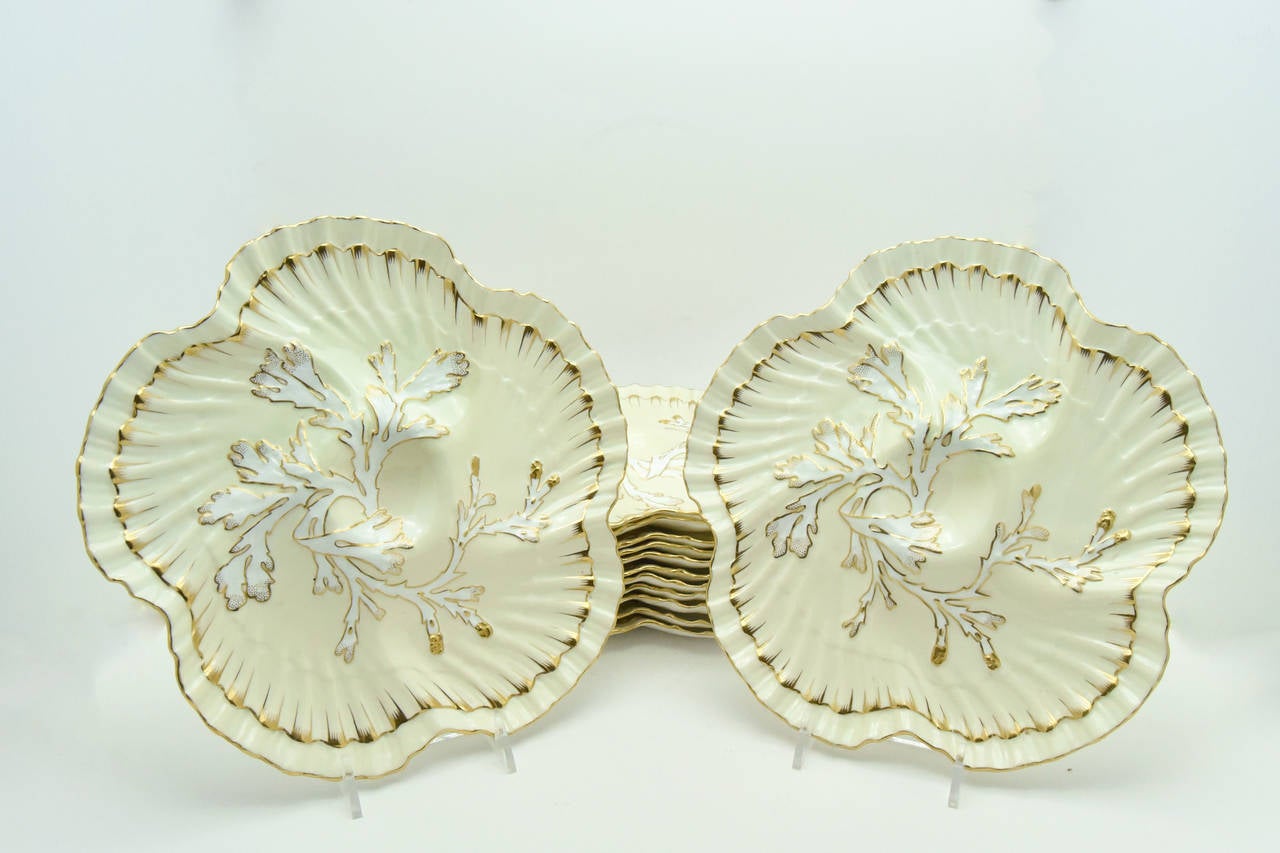 This unique set of 12 Aesthetic Movement, Brownfield's for Tiffany, oyster plates features a delicate shaped edge reminiscent of scallop shells with a coral design at the center to complete the nautical look. The gold trim over ivory, highlights the