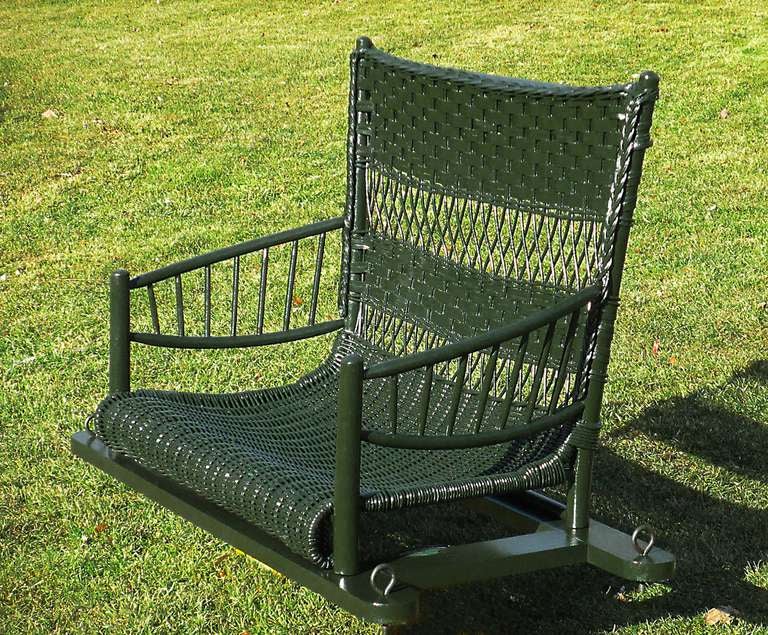 Wicker porch swing in dark green painted finish having Adirondack style features.  Back panel with combination of closely woven basketweave pattern alternating with open lattice work.  Solid woven seat with serpentine roll to front.  Curved wooden