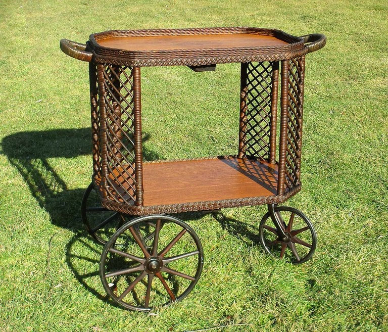 Bar Harbor style wicker tea cart having 2 large wood-spoked wheels and a small pivoting wheel. Handles at both ends for smooth rolling in any direction.  Hallmark Bar Harbor criss-crossed lattice design to 4 angled corner panels. Two quarter sawn