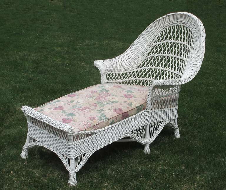 Bar Harbor style wicker chaise lounge in white painted finish.  High arched back, wide flared arms, & unusual rolled foot gallery.  Arched skirting with pine-apple twist-wrapped feet.  Coiled spring seat platform.