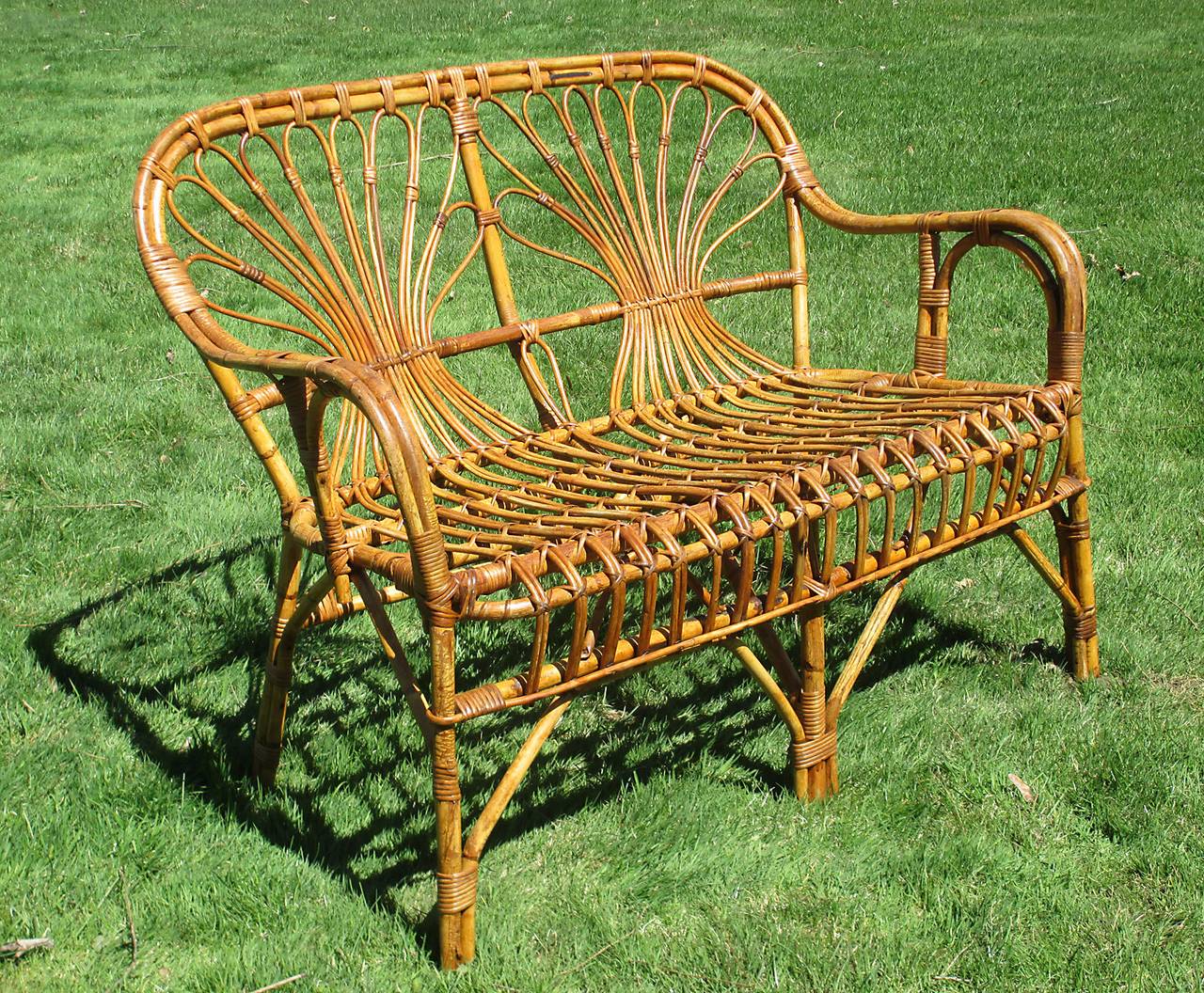 Stick Wicker settee in honey-toned natural stained finish.  Back panel having looped rattan strands with decorative pinching at center, continuing from back to seat and curved front skirt.  Last photo shown with complementing armchairs listed &