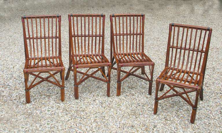 Set of four Stick Wicker dining chairs in natural stained finish with red & black painted bandings.  Large scale squared back form with ample seating area.  Suitable chairs for dining or use at a game table.