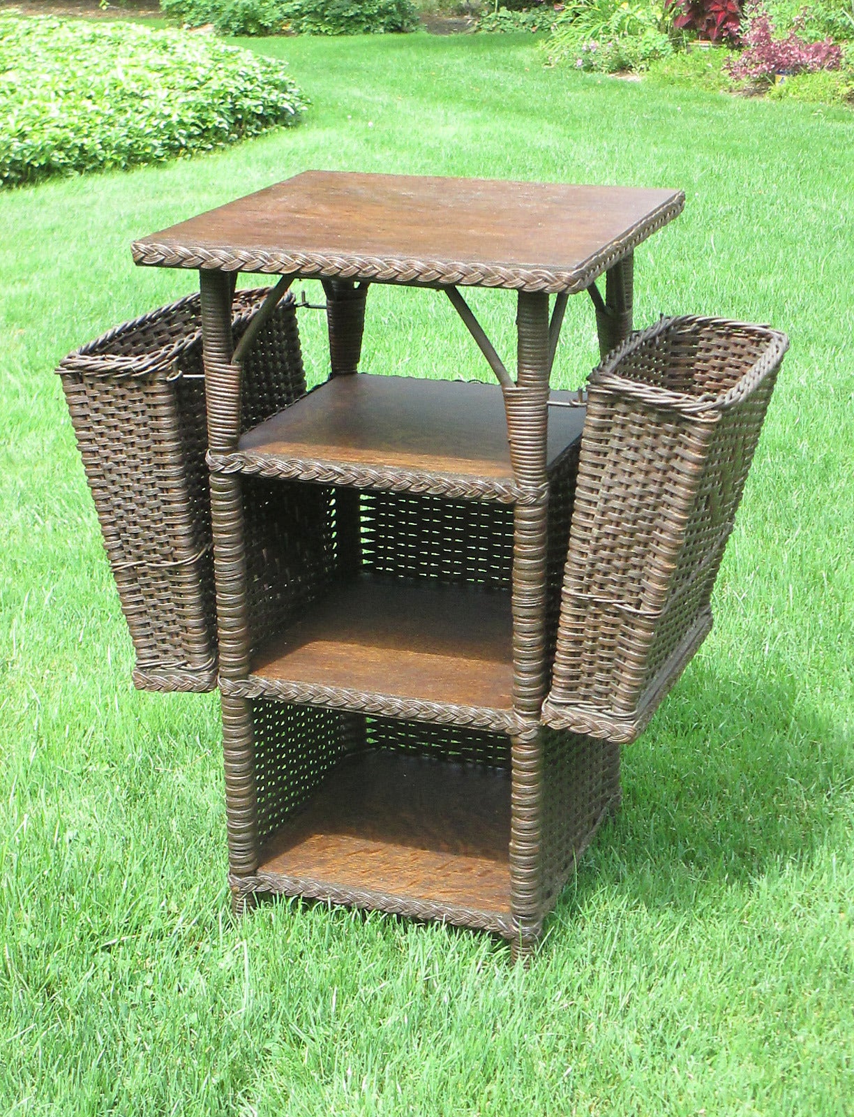 Wicker bookshelf/end table in original dark stained finish.  Wood top & three shelf surfaces constructed of solid oak.  Sides feature removable wicker magazine baskets having Art Deco woven diamond patterns.  Table itself has the hallmark woven