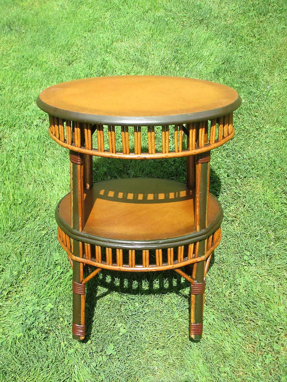 Round Stick Wicker table in original faux-natural finish with dark green glazed trim.  Wood top & bottom shelf with paired reed aprons.  Handy portable tea table height size.