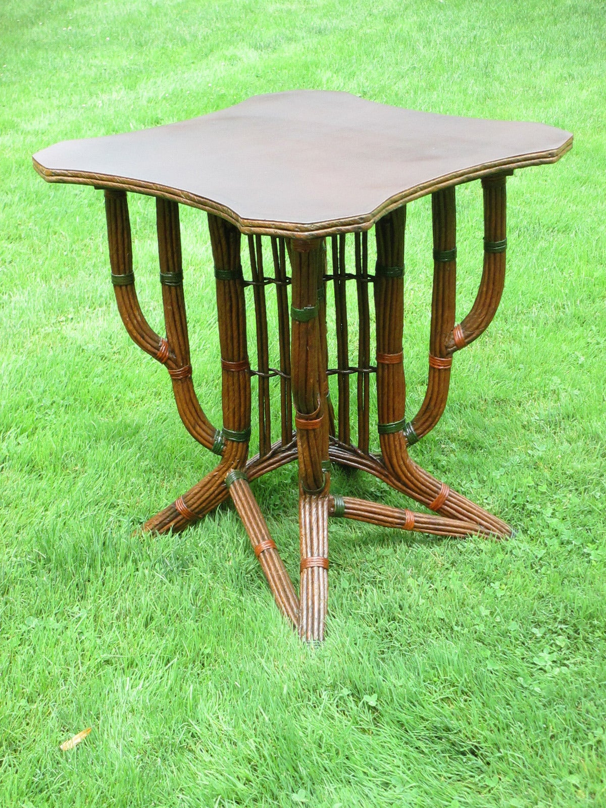Unconventional Art Deco wicker table in natural stained finish with green and cinnamon painted trim. Artistically shaped base with multiple stacked fiber rush strands creating a unique stylized 