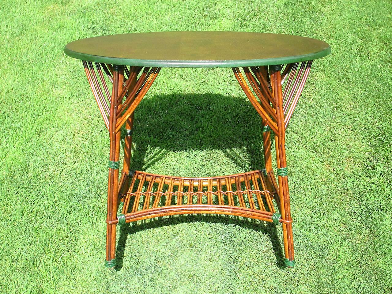 Oval Stick Wicker table in rich toned natural stained finish with green glazed trim.  Wood top with v-shaped rattan strands atop each leg.  Arched rattan bottom shelf.