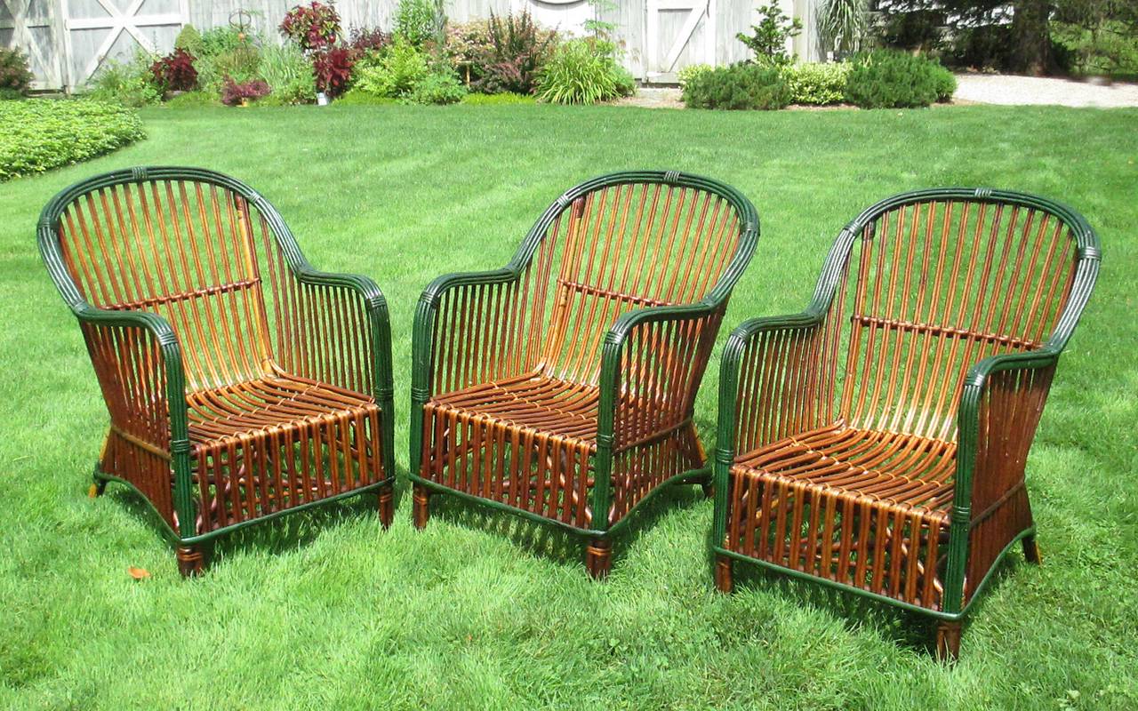 Set of three matching Stick Wicker chairs in rich natural stained finish with green glazed trim.  Closely paired rattan strands overall with stacked rattan arms.  Comfortable forms having gently sloped seats and arms.