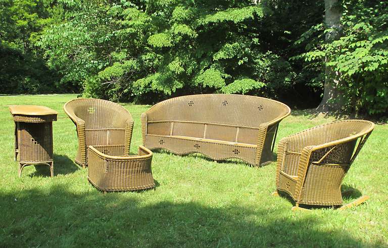Five-Piece Art Deco wicker set having strong Mission style influence to decorative cut-outs in solid woven panels. Original  honey-toned painted & glazed finish.  Large sofa, chair with ottoman, rocker & console table.  Measurements as follows -