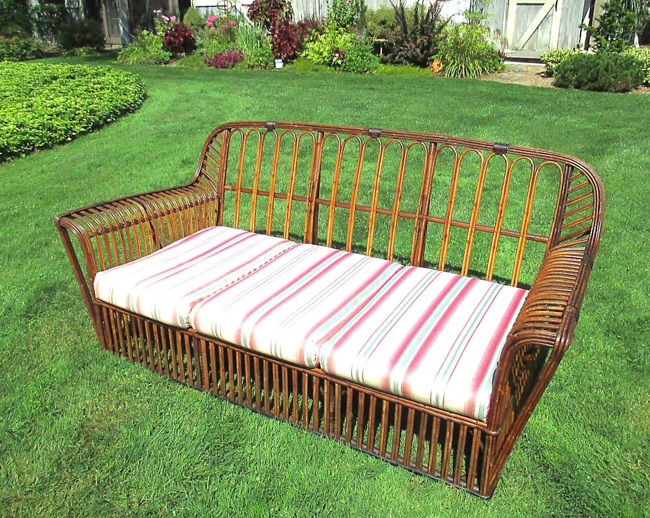Stick wicker sofa in natural stained finish with cinnamon and black painted trim. Rounded back form with gently arched armrests. Paired vertical rattan strands to front and sides, looped strands to back. Newer foam seat and back cushions.