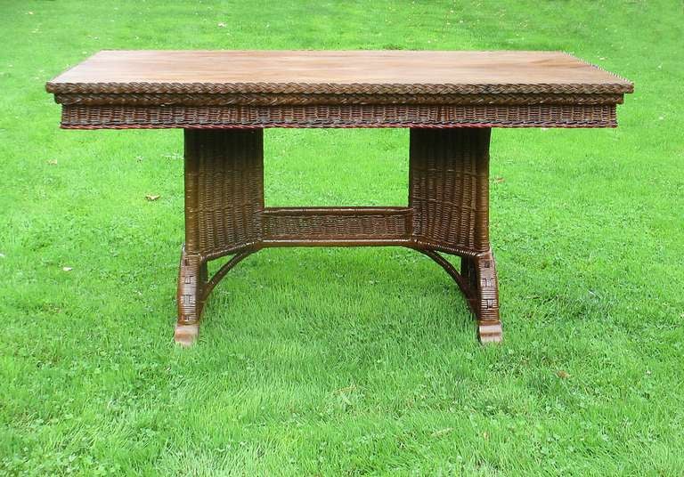 Art Deco wicker library/dining table in bronze-toned painted finish with red & black trim & natural stained oak top.  Trestle base with double pedestals having cut-outs and decorative arched woven panels supported on oak bracket based feet.  Large