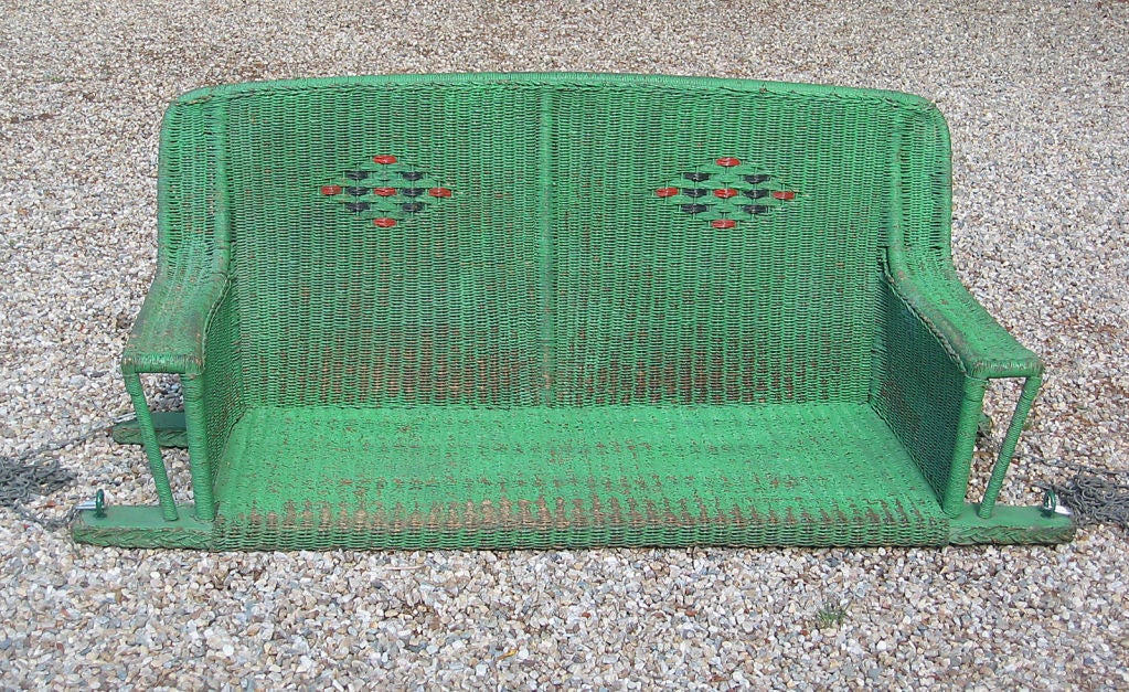 Art Deco style wicker porch swing in worn green painted finish with red & black detail to woven diamond designs. (can be re-painted any color on request)  Wide flat arms, ample seating area for two.