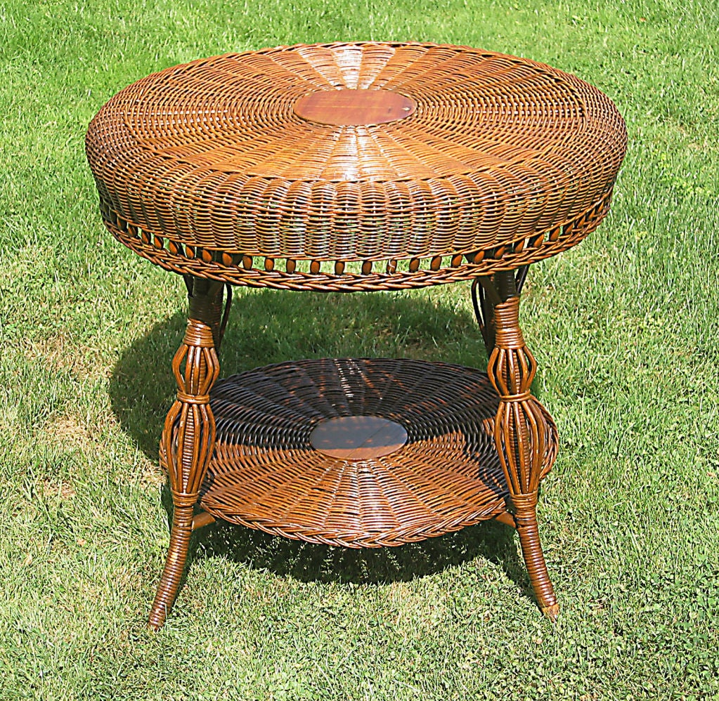Round Victorian wicker table with large serpentine rolled apron having decorative wooden balls. Full bottom shelf with braided border. Weave on both surfaces radiates from 8