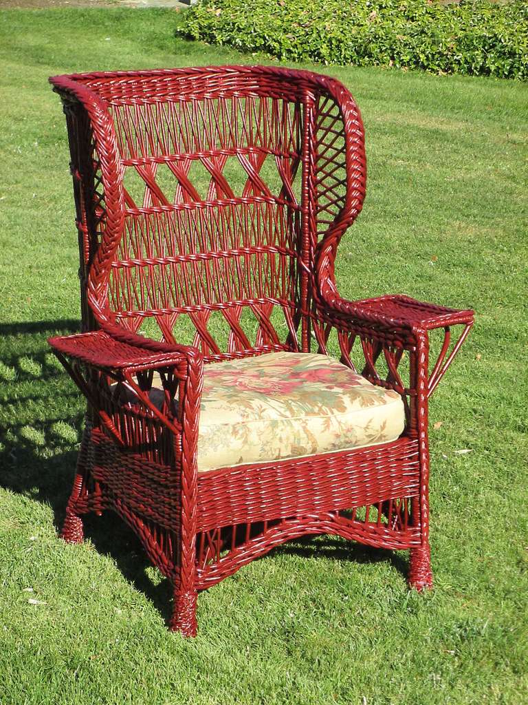 Bar Harbor style wicker wingback armchair in red painted finish. (Can be re-painted any color on request.) Series of woven three-strand XXX's referred to as Cape May design. High level back, enveloping wings, wide flat arms. Four pineapple feet. 