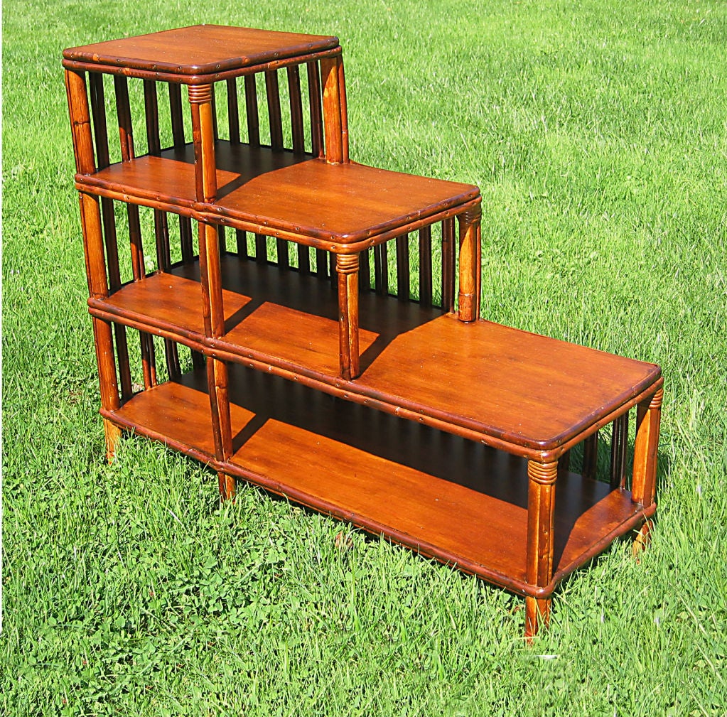 Stick Wicker bookcase end table having four shelves of staggered length.  Open front & one side, hallmark paired vertical reeds on back & other side.