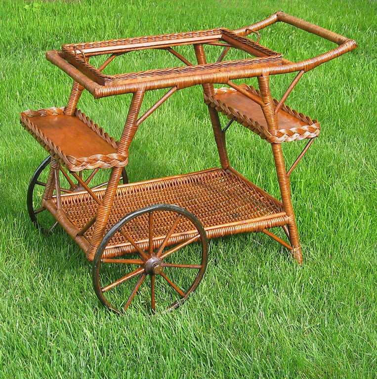 Wicker teacart in natural stained finish.  Removable serving tray, two stepped out wood shelves framed in braiding, woven bottom storage shelf and large wheels with wooden spokes.