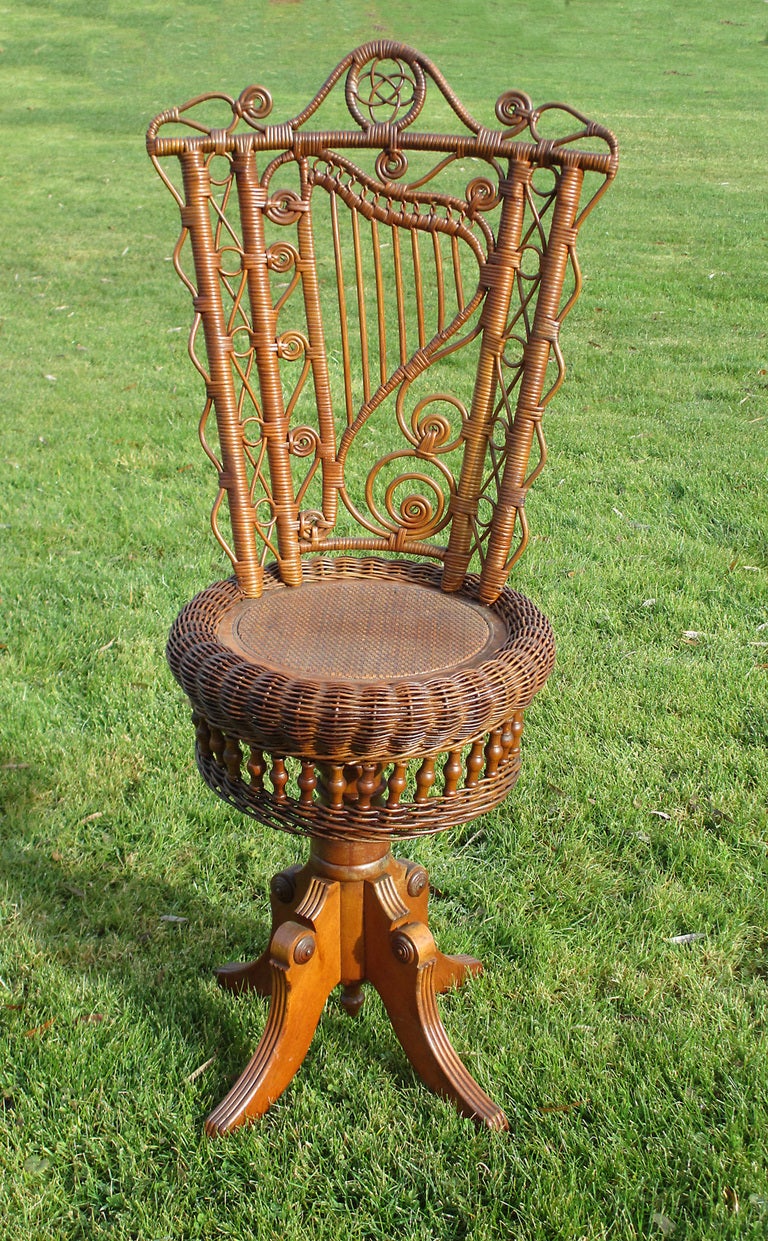 Victorian revolving wicker piano stool in original natural stained finish.  Harp motif woven into the backrest amid curlicues, reed loops, and scalloping.  Round pressed cane seat framed in serpentine roll, followed by beadwork embellishments on