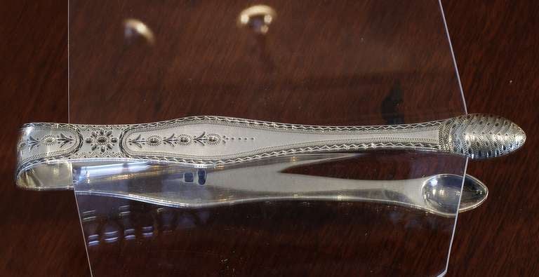 Sterling sugar tongs with all over brite cut engraved decoration made by Samuel Godbehere and Edward Wiggens whose maker's
mark was entered in 1785. Though the touch marks show the lion and king's head there is no date mark. Stylistically it would