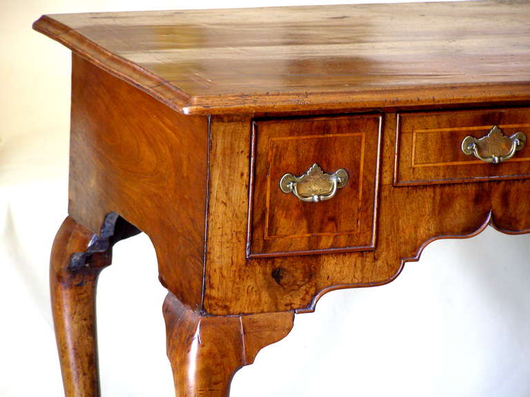 A very nice quality period early 18th century small lowboy. The walnut has faded to a light to medium honey color and still retains some very early finish on the sides of the case, the drawer fronts and the facade of the front. The hardware except