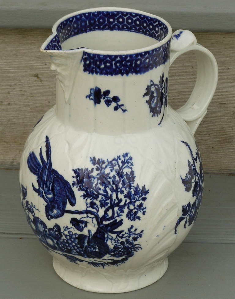 A very good large example of early Worcester semi-porcelain. 
The general type is referred to as a mask spout and cabbage leaf molded jug. The decoration is known as the parrot and fruit or the parrot pecking pattern.