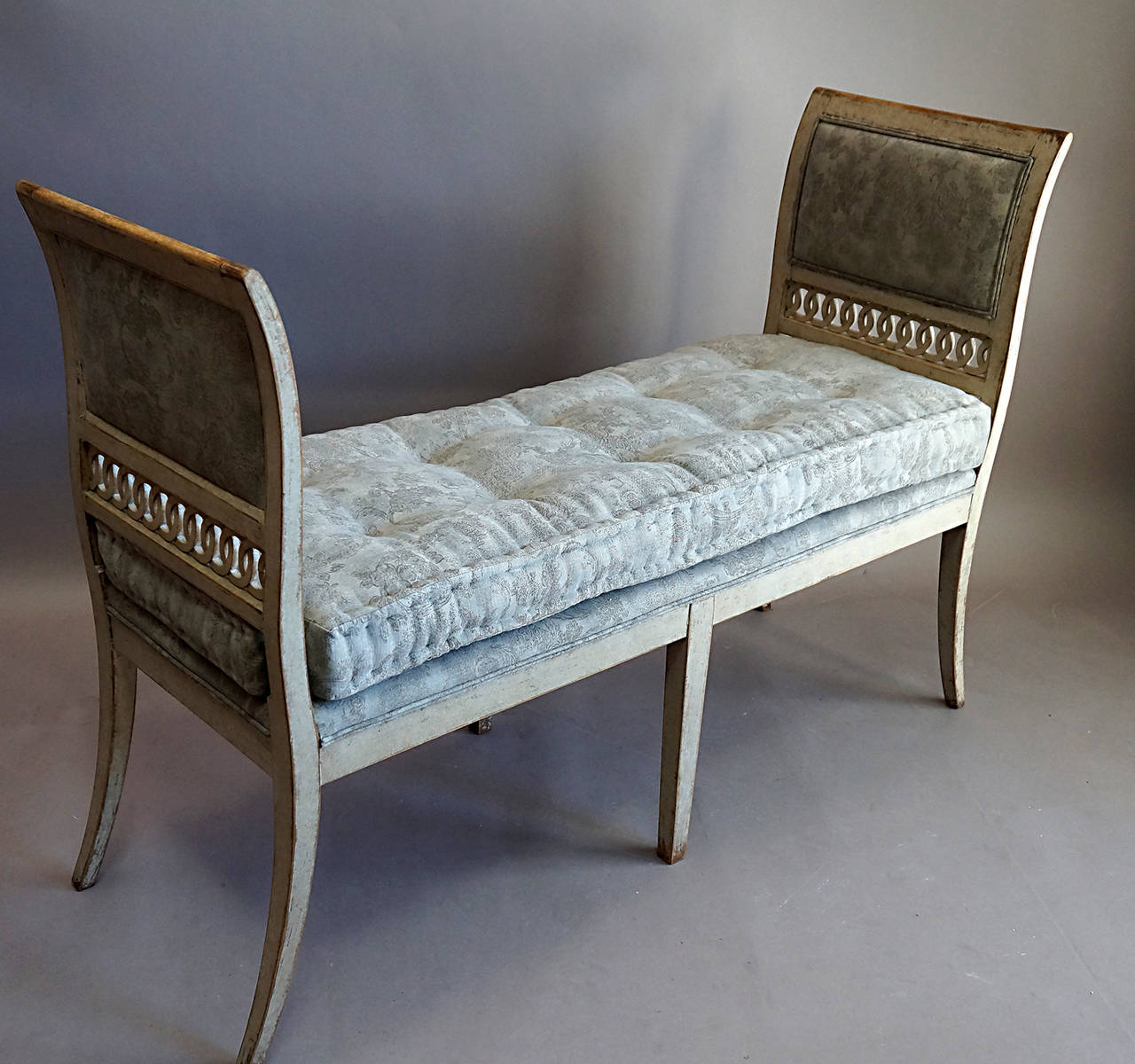 Gustavian window bench with curved, upholstered arms with pierced detail extending into saber legs. The arms and the loose cushion are newly covered with a beautiful gray printed cotton.