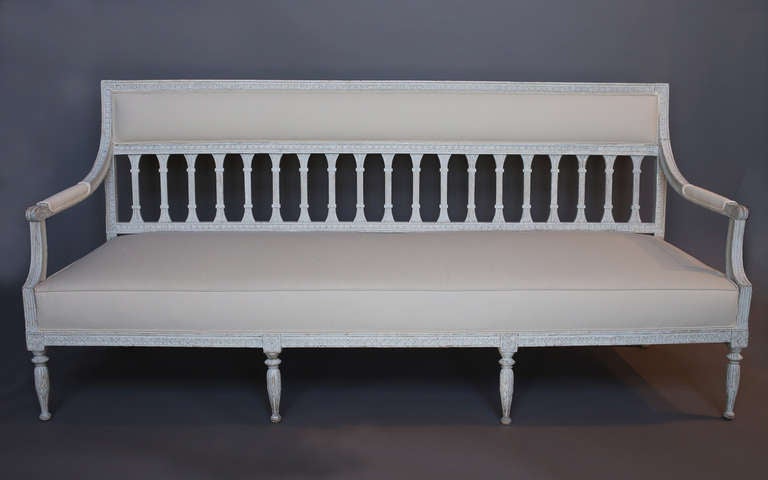 Gustavian bench, Sweden, circa 1790, with a Stockholm hallmark and retaining its original painted surface. Egg and dart molding surrounds the seat and the back, running down the arms to the upholstered rests. Simplified acanthus leaf carving