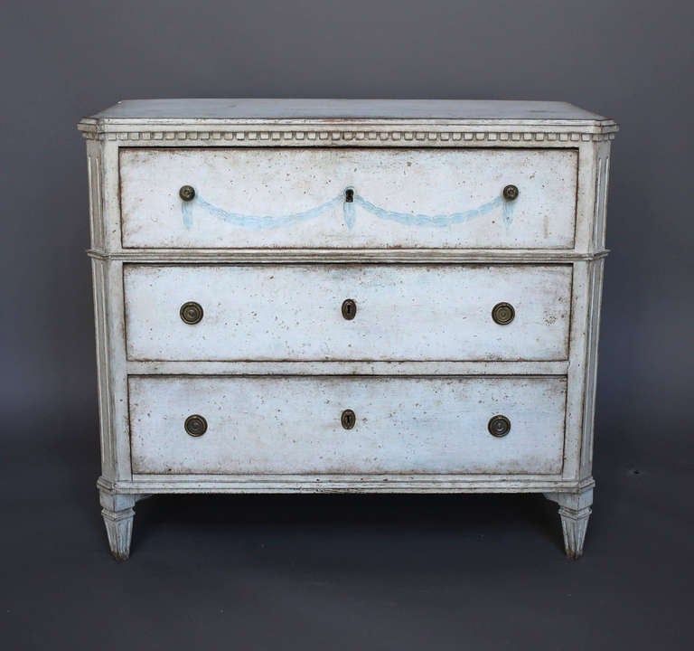 Period Gustavian chest of drawers, Sweden circa 1810, with canted corners, dentil detail under the shaped top, and brass hardware. The front and sides are decorated with painted swags in a pale Swedish blue.