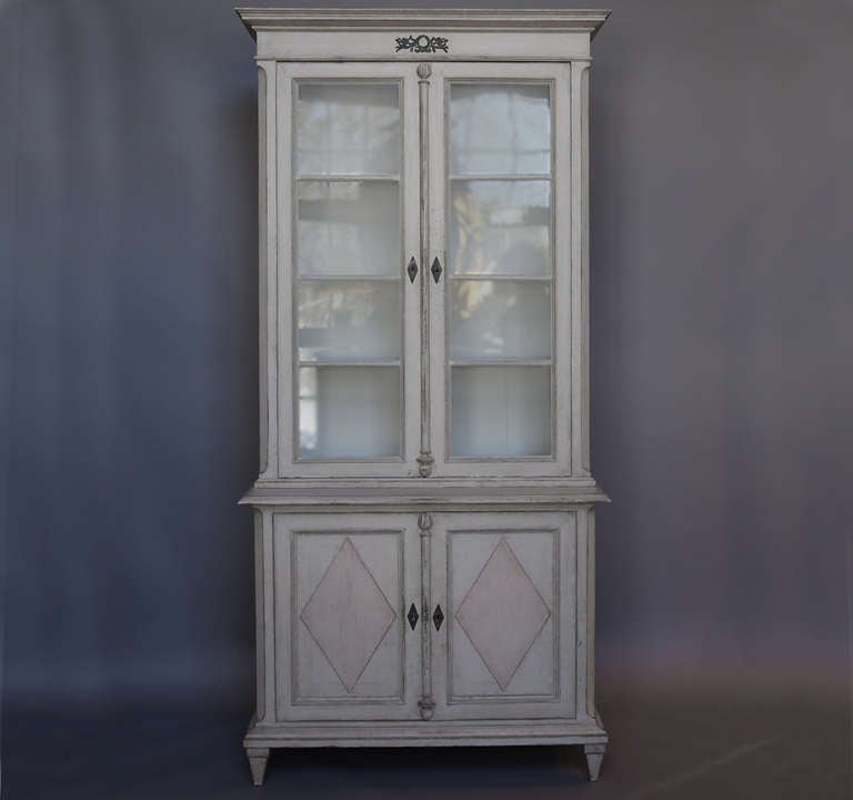 Period Gustavian library cabinet, Sweden circa 1820, with three shelves in the upper section behind original glass. The separate lower section has raised lozenges on the two doors with a single shelf inside. The applied bronze decoration at the top