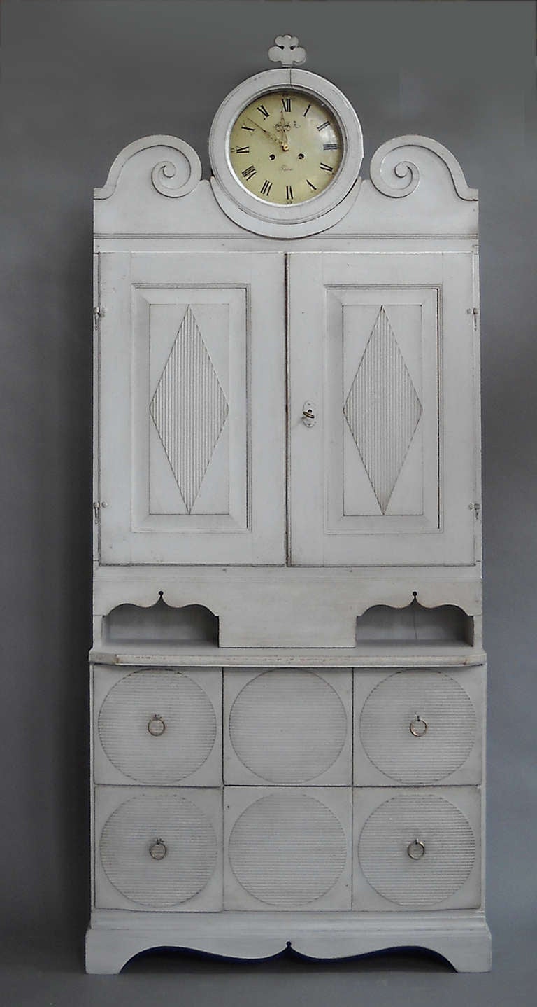 Unusual Gustavian cabinet with integral clock, Sweden circa 1810. Certainly a rural interpretation of the popular urban pieces of the period, the upper cabinet doors have raised, reeded lozenges and interior shelves on either side of the chase for