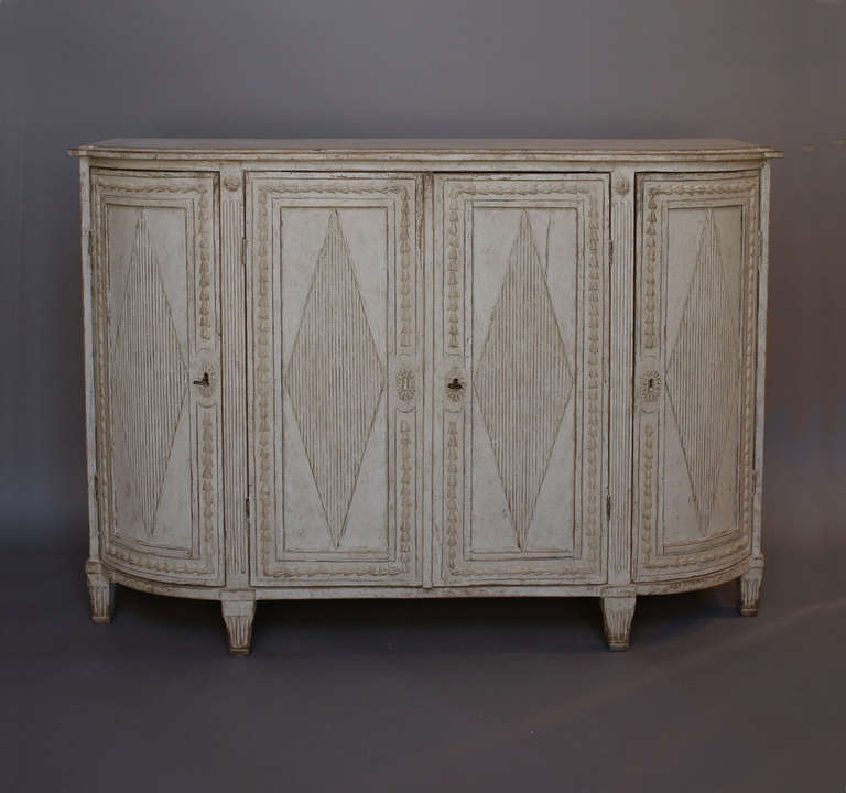 Four door Gustavian sideboard with rounded ends, Sweden circa 1810. Each door has bell-flower carving surrounding a raised reeded lozenge. The central section has two shelves and two drawers with fluted fronts. The side sections also have two