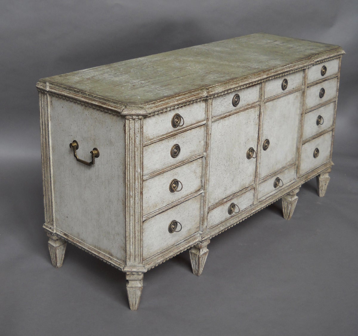 Early Gustavian sideboard, Sweden, circa 1790, with later white paint, green top and brass hardware. A bank of four drawers under dentil molding span the top, with a bank of three graduated drawers on either side of a central storage compartment.