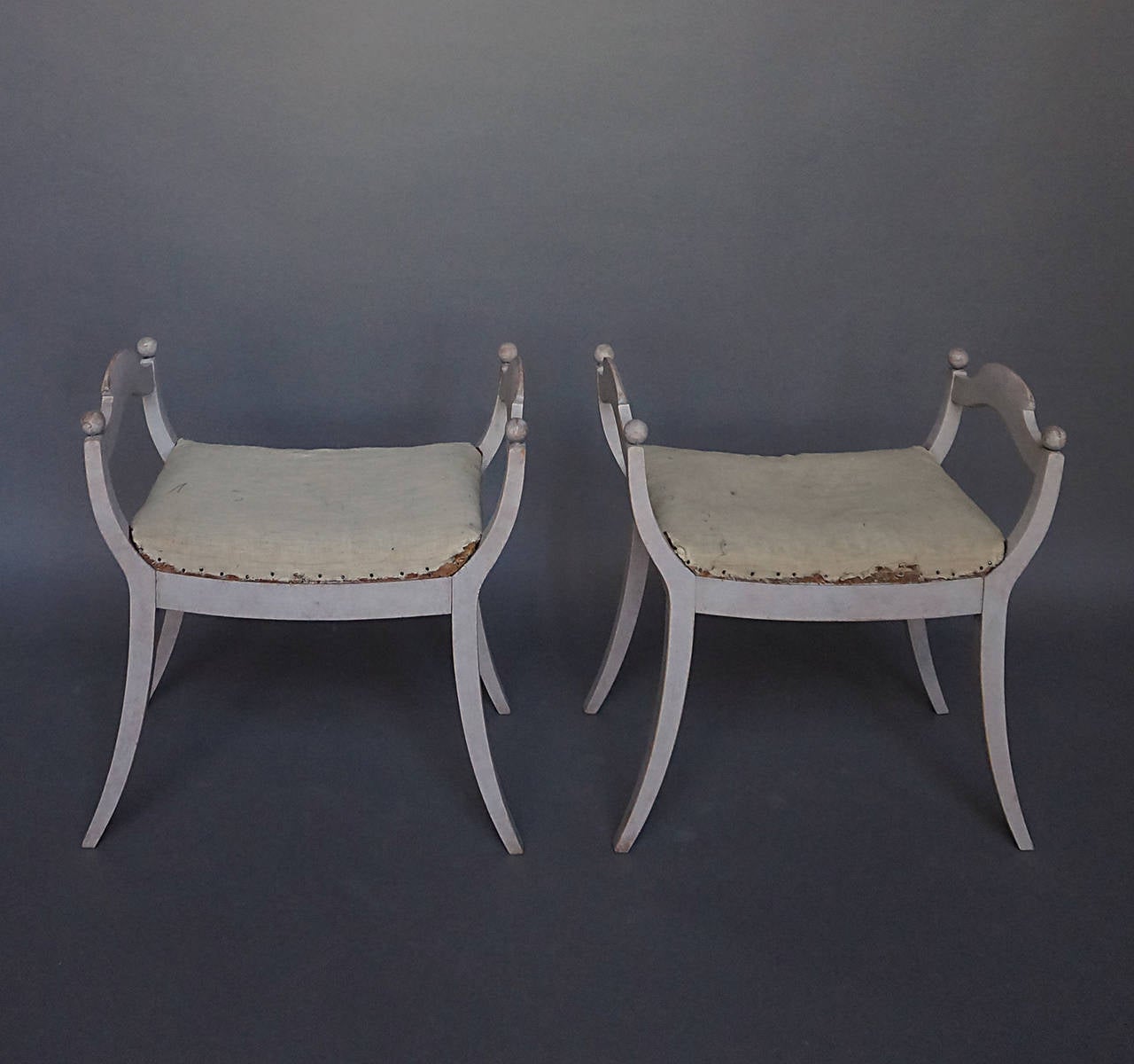 Pair of stools in the neoclassical style, Sweden circa 1910, with upholstered seats, shaped armrests, and saber legs. Sturdy and quite comfortable.