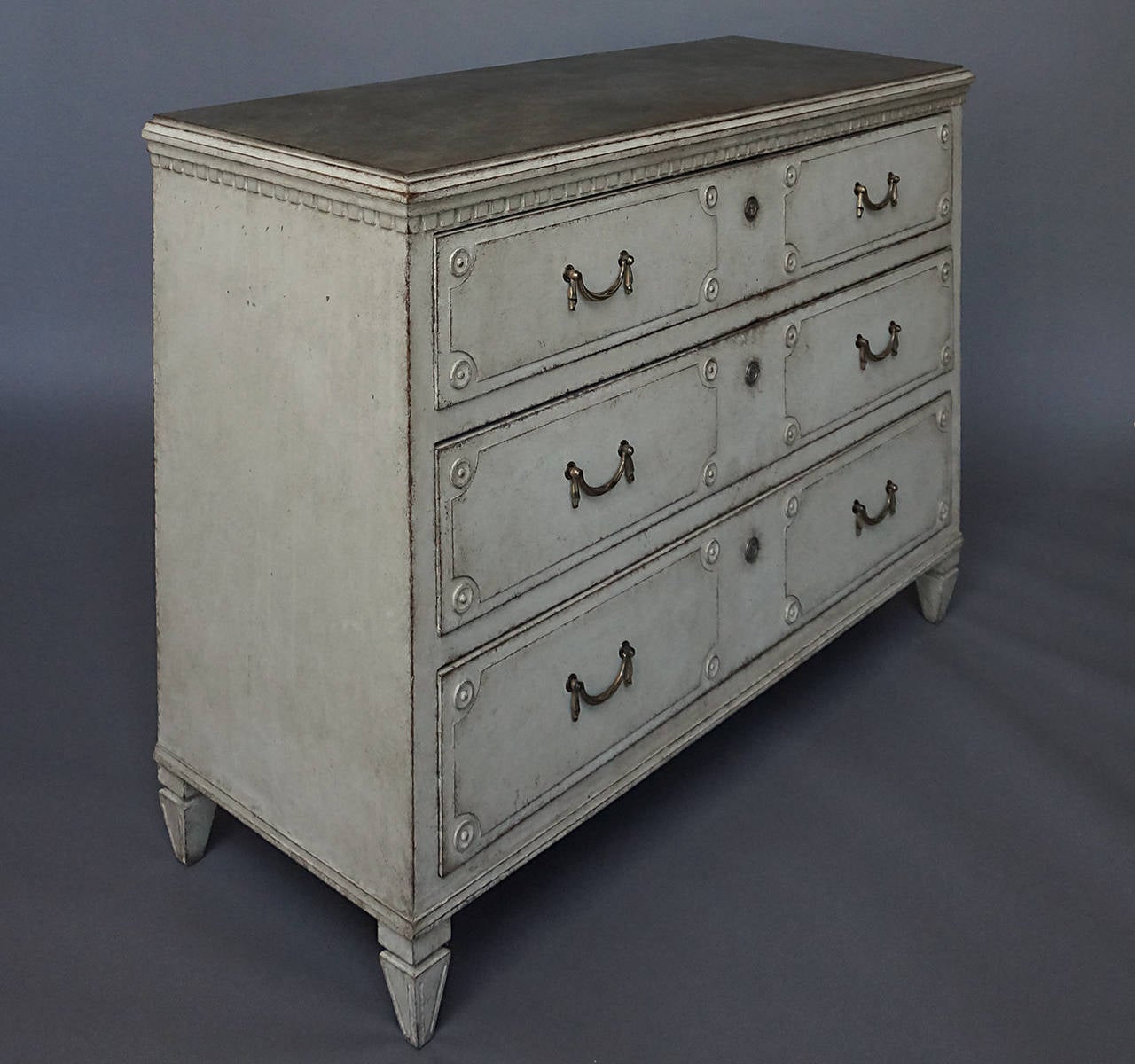 Swedish chest of drawers, circa 1870, with original swagged brass hardware. Dentil molding under the marbleized top and three drawers each having two raised panels with rondels inset at each corner.