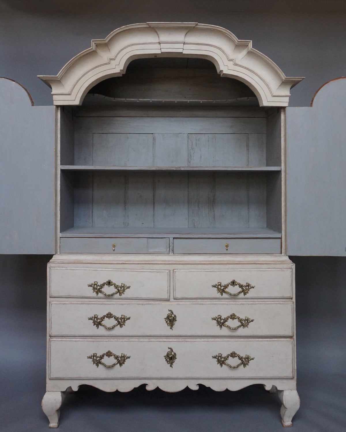 Swedish Rococo cabinet in two parts, circa 1760, with original hardware. The upper section has two shelves and two drawers behind double doors, all under an arched cornice. The lower section has two over two drawers on a shaped base with compressed