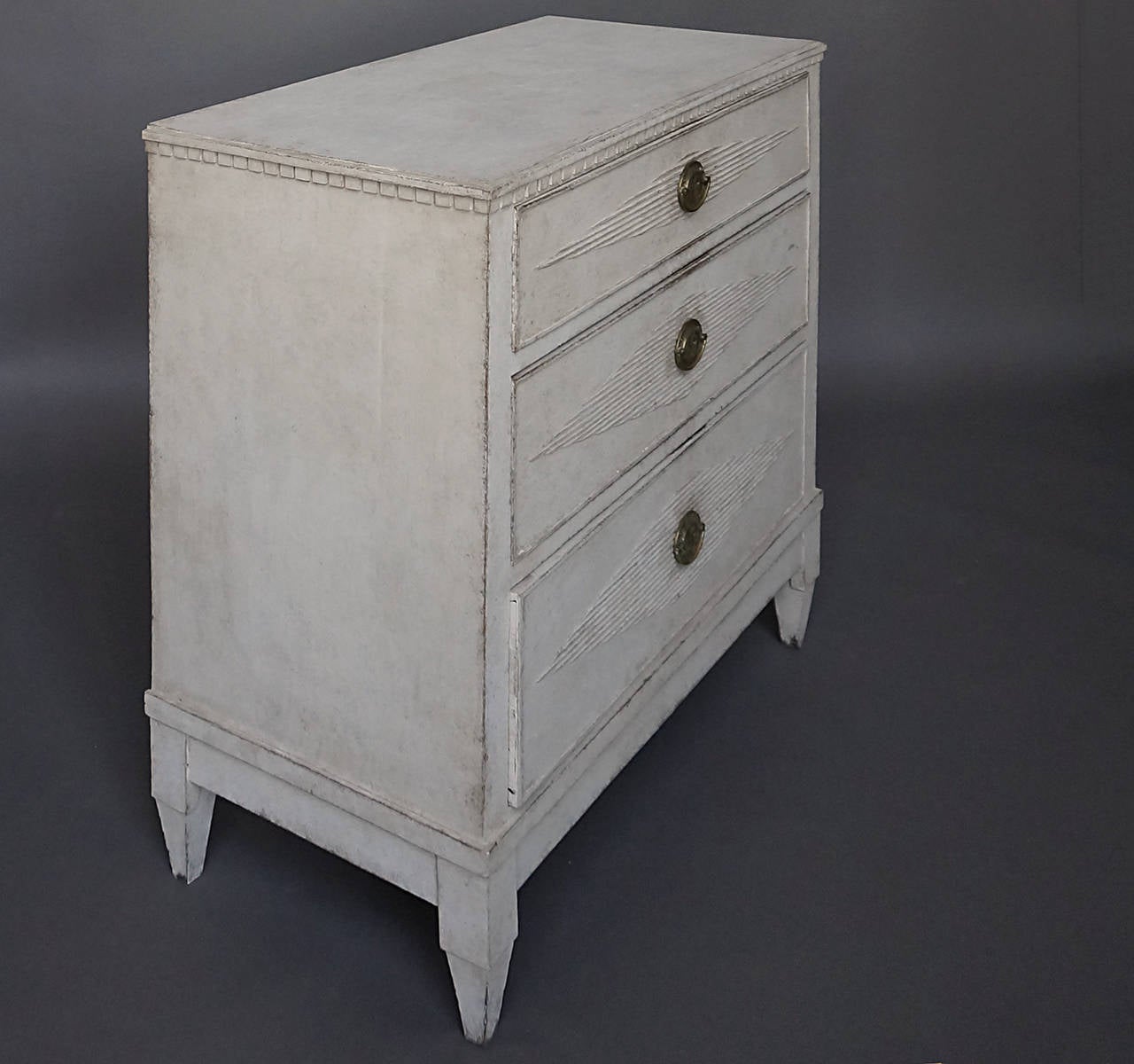 Period neoclassical commode, Sweden, circa 1840, with dentil molding under the top and a raise, reeded lozenge on each of the three drawers. Original brass hardware.