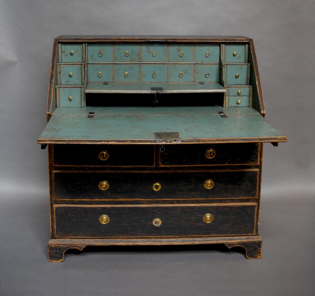 Oak and pine writing desk in black paint, Sweden circa 1770. The body of the desk has one over two over two drawers, all with brass hardware. Behind the slant top are two banks of three small drawers on either side of a locking fall front. Behind